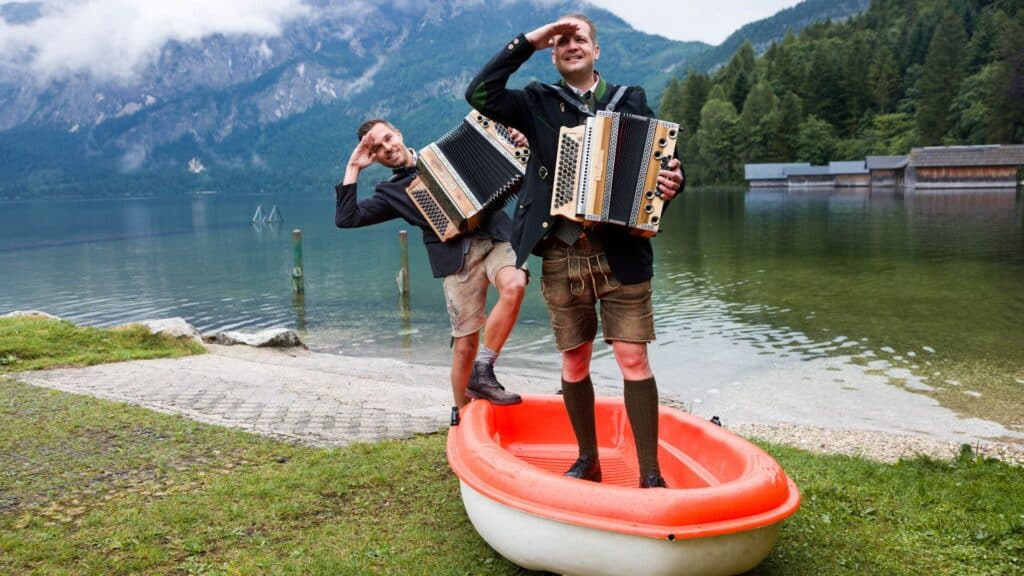 Richi und René Kogler stehen in einem Boot, um zu verdeutlichen, wie eine Harmonika auf Reisen transportierbar ist